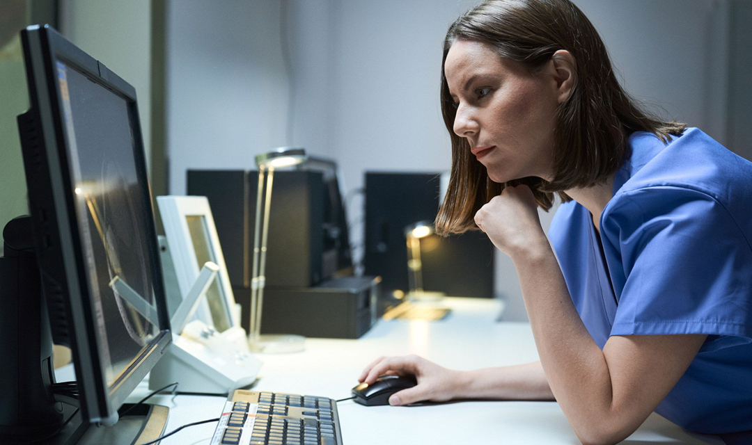 Female in scrubs looking at a computer monitor